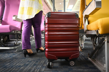 Cropped shot of 60s female tourist with suitcase walking the aisle on plane. Travel and summer...