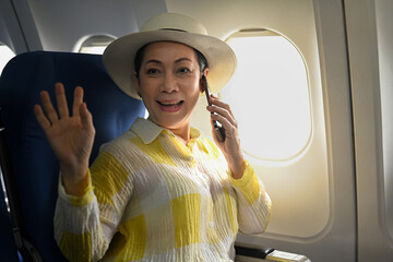 Positive middle aged woman tourist passenger talking on mobile phone and waving hand to camera