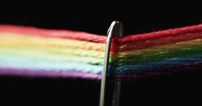 Video of micro of rainbow coloured threads going through needle with copy space on black background