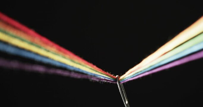 Video of micro of rainbow coloured threads going through needle with copy space on black background