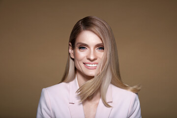 Fototapeta premium Portrait of stylish attractive woman with blonde hair smiling on pastel brown background