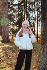 Portrait of stylish teen cover girl model in white autumn jacket posing at fall park outdoor, thought looking. Lovely young lady walking in autumn forest. Leisure activity concept. Copy ad text space