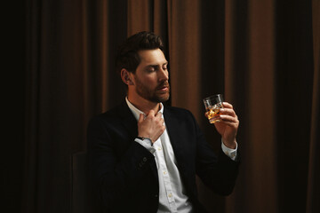 Man in suit holding glass of whiskey with ice cubes on brown background