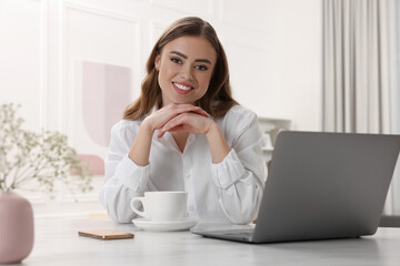 Happy woman with laptop at white table in room