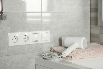 Power sockets, light switches on wall near table with hairdryer and towel indoors