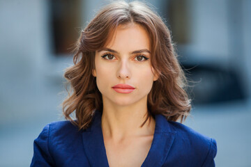 Portrait of a beautiful young woman with long brown hair, dressed in a blue jacket, standing against the background of an office building. strong and confident business woman