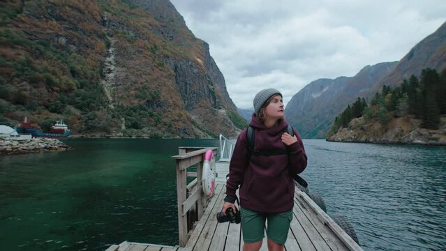 Female travel photographer walk on pier in scenic surroundings. Norwegian fjord in autumn fall colors. Inspiring adventure blogger create content for social media or travel agency