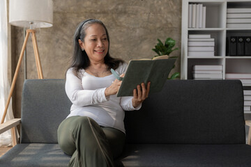 Asian senior woman reading a book on the sofa at home Activity ideas for the elderly in the family.