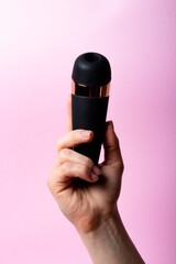 Female hand is holding black vacuum clitoral stimulator on a pink background. Place for text. Sex shop concept. Copy space