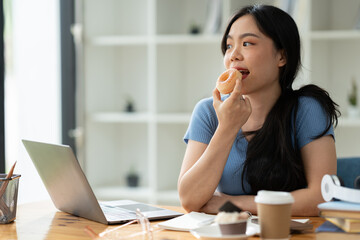A cute and happy Asian woman having fun. Relax eating donuts at your desk at home. holiday concept,...