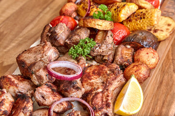 Part of the wooden board with fried meat and vegetables on the wooden table, close-up, shallow depth of field. Beef meat in focus