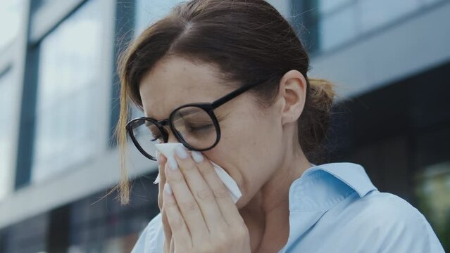 Anxious woman suffering rhinitis, sneezing and blowing nose to paper napkin