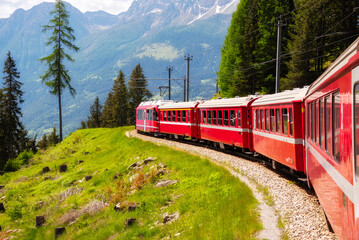 Red train moving in beautiful green summer forest in Switzerland