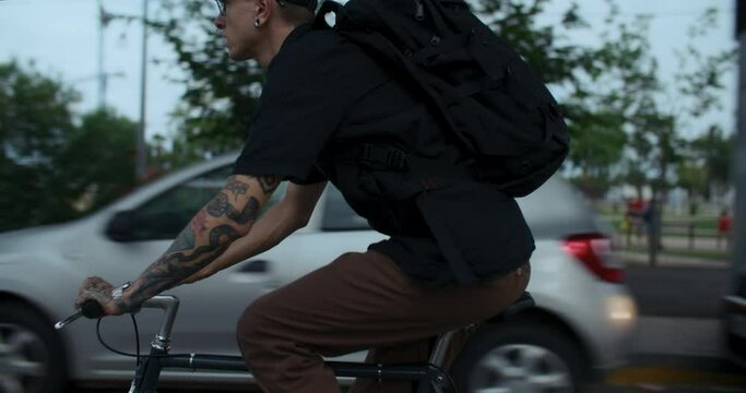 Side shot of young man ride his bike in city on urban mobility bike lane. Modern hipster millennial guy pedal on single speed commuter bike on way to work or school