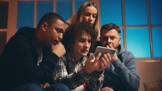 Group of multiethnic friends watching sports game on smartphone, rejoicing goal