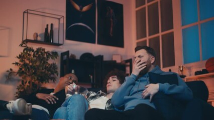 Relaxed multiethnic male friends watching boring tv show and talking at home