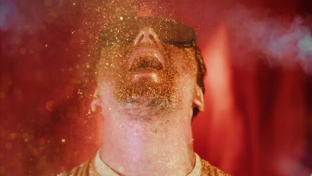 Crazy fun man sprinkles himself with sparkle particles. Fun video, funny face, tongue out. Comical funny portrait guy in sunglasses pouring on face and mouth gold glitter in super slow motion 1000fps
