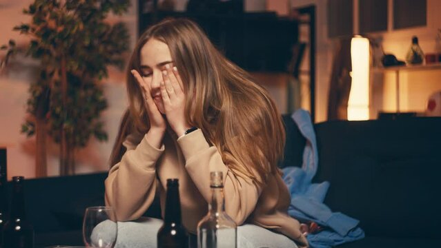 Young drunk woman sitting on couch after home party, feeling dizzy and hangover