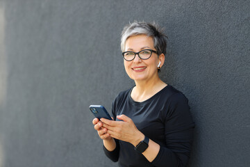 Modern mature sporty woman using smartphone in the city. A blend of technology and fashion, embracing an active lifestyle.
