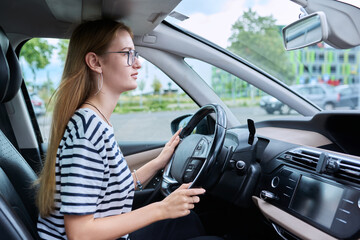 Fototapeta na wymiar Teenage girl driver in glasses sitting behind wheel of car