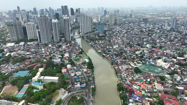 Manila cityscape at river banks aerial. Downtown area with cottages, skyscrapers, buildings. Urban Philippines city scape with streets and roads. Town drone shot. Poor Homes Along Rich Skyscrapers.
