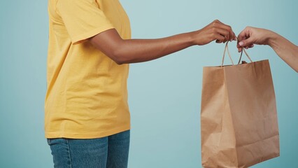 Closeup shot. Delivery woman in uniform giving female client paper bag. Isolated on blue background.