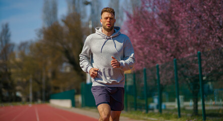 Fototapeta premium A man in a gray hoodie is jogging at a sports stadium.