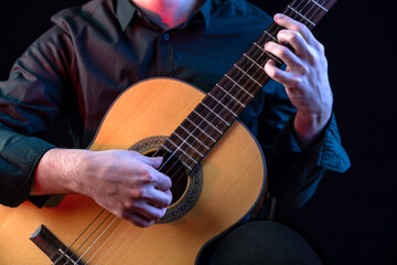 Fototapeta na wymiar The guy in the dark shirt is plucking the strings of a six-string guitar