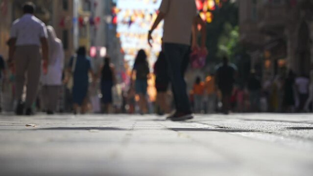 Low-angle close up of blurred people crowd feet walking by paving slabs on pedestrian street . Popular Istiklal Avenue leading to Taksim Square. Istanbul, Turkey
