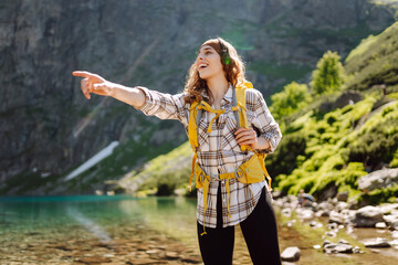 Female tourist with a bright yellow backpack stands near a alpine lake in the midst of mountain landscapes. Concept of tourism, travel, hiking.