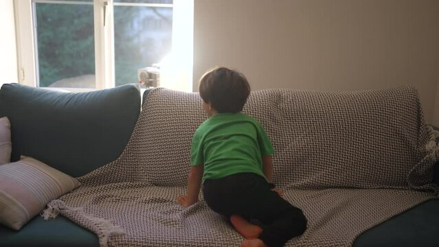 Child having fun at home jumping into couch in the evening. Young boy diving into sofa with pillows