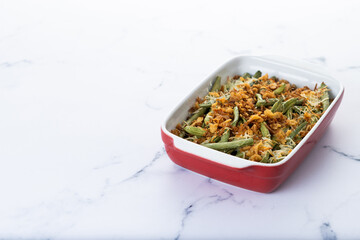 A traditional green bean casserole topped with French Fried Onions and cream of mushroom on white marble. Copy space