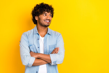 Portrait of pleasant man with wavy hairstyle wear jeans shirt arms folded look at sale empty space isolated on yellow color background