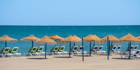 Beautiful sandy beach with palm tree umbrellas and sun loungers