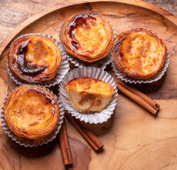 Pastel de nata tarts and cinnamon sticks on wooden tray. Top view.