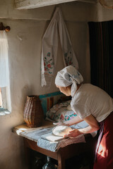 A woman in traditional Ukrainian clothing kneads bread dough.