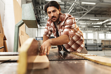 Young carpenter working on woodworking machines in the furniture factory