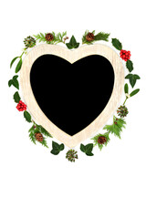 Christmas heart shape wreath with holly, mistletoe traditional winter greenery. Romantic symbol for the festive holiday season on white background with chalkboard. 