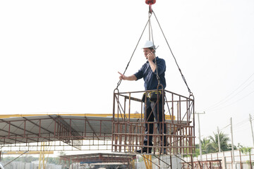 Naklejka na ściany i meble Foreman construction builder worker wearing safety uniform, helmet working on lift basket at construction site