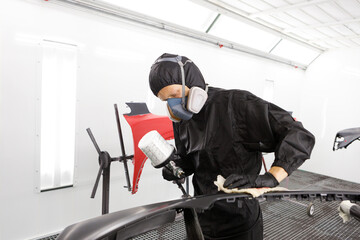 Automotive paint services, quality auto body shop concept. Male car mechanic working with spray gun...