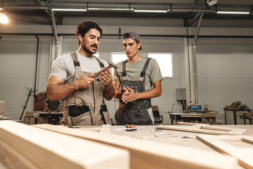 Two young men carpenters making furniture in warehouse of wood factory