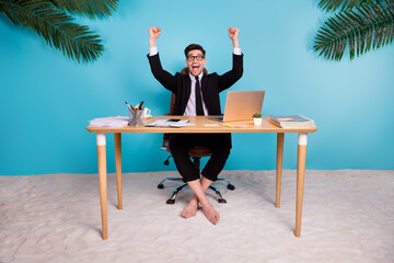 Photo of crazy marketer guy sitting table raise fists up win summer vacation isolated on blue color...