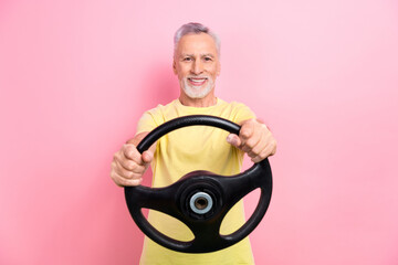Photo of satisfied positive man with gray beard dressed yellow t-shirt hold steering wheel test new car isolated on pink color background