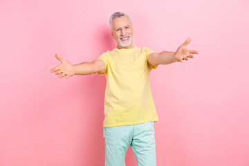 Photo of friendly cheerful senior man with white beard dressed yellow t-shirt stretching hands to...