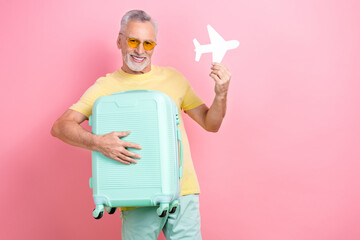 Photo of satisfied optimistic man with beard dressed yellow t-shirt holding small paper plane valise isolated on pink color background