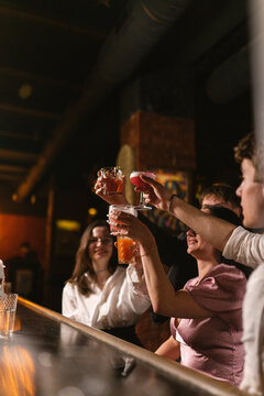 Guys treat brunette girls with alcoholic cocktails at bar counter. Young people relax and enjoy fun party in cozy restaurant