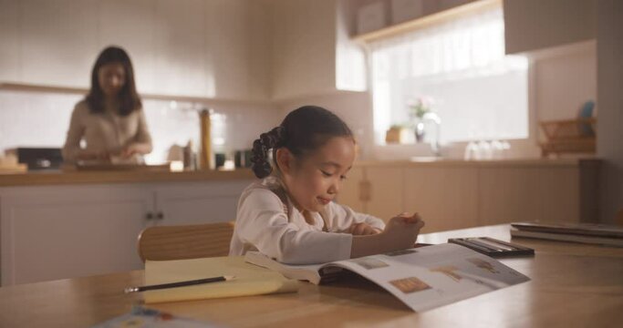 Portrait of a Korean Female Child Sitting at a Kitchen Table and Drawing While her Mother is Preparing Breakfast. Little Cute Girl Waiting for Nutritious Meal Before Going to School