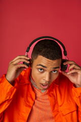 stylish african american man listening music in wireless headphones on red background