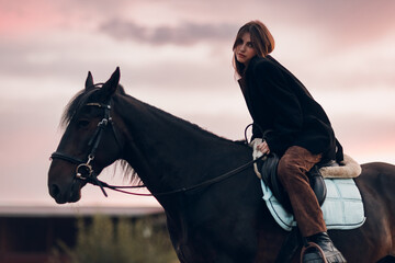 Young woman in black with her horse at sunset outdoors