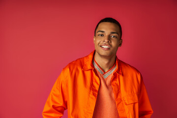 handsome african american guy in trendy orange shirt, with radiant smile looking at camera on red